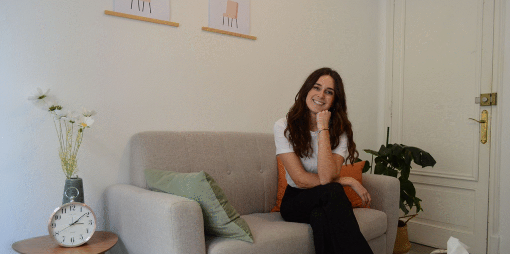Laura sentada con las piernas cruzadas en el sofá mientras apoya la cabeza sobre su puño y sonrie